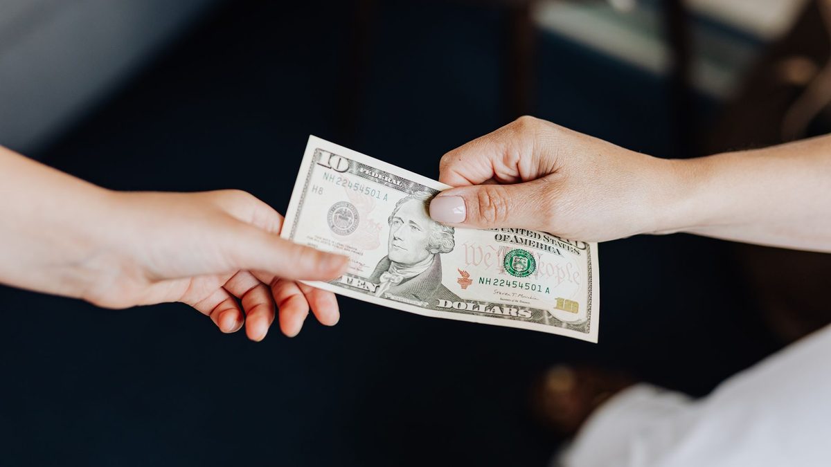 Two people exchanging a ten dollar bill in a close-up hand-to-hand transaction.