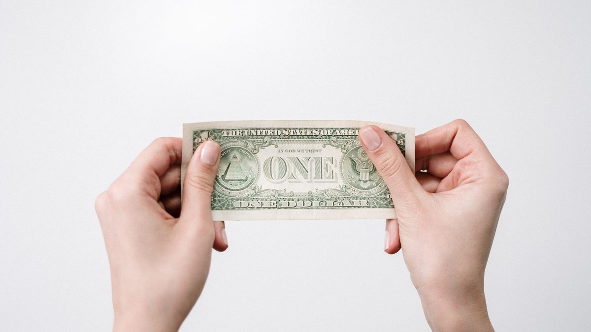 A close-up image of hands holding a one dollar bill, symbolizing finance and economy.