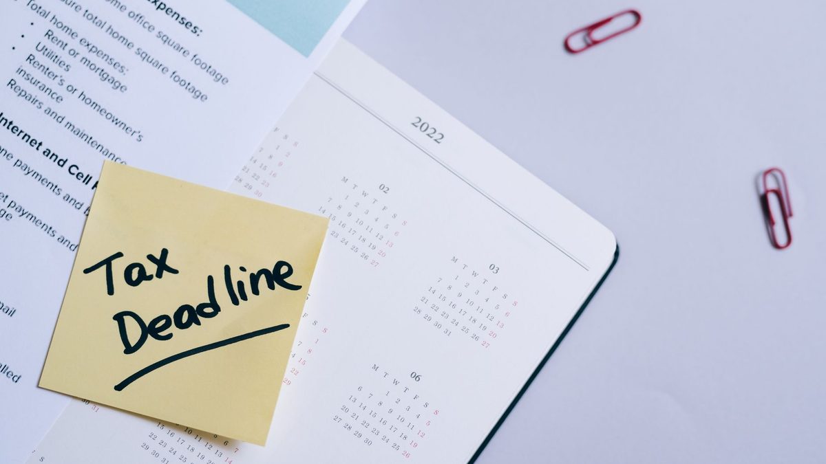 A sticky note highlights tax deadline on a calendar alongside documents, emphasizing financial planning.