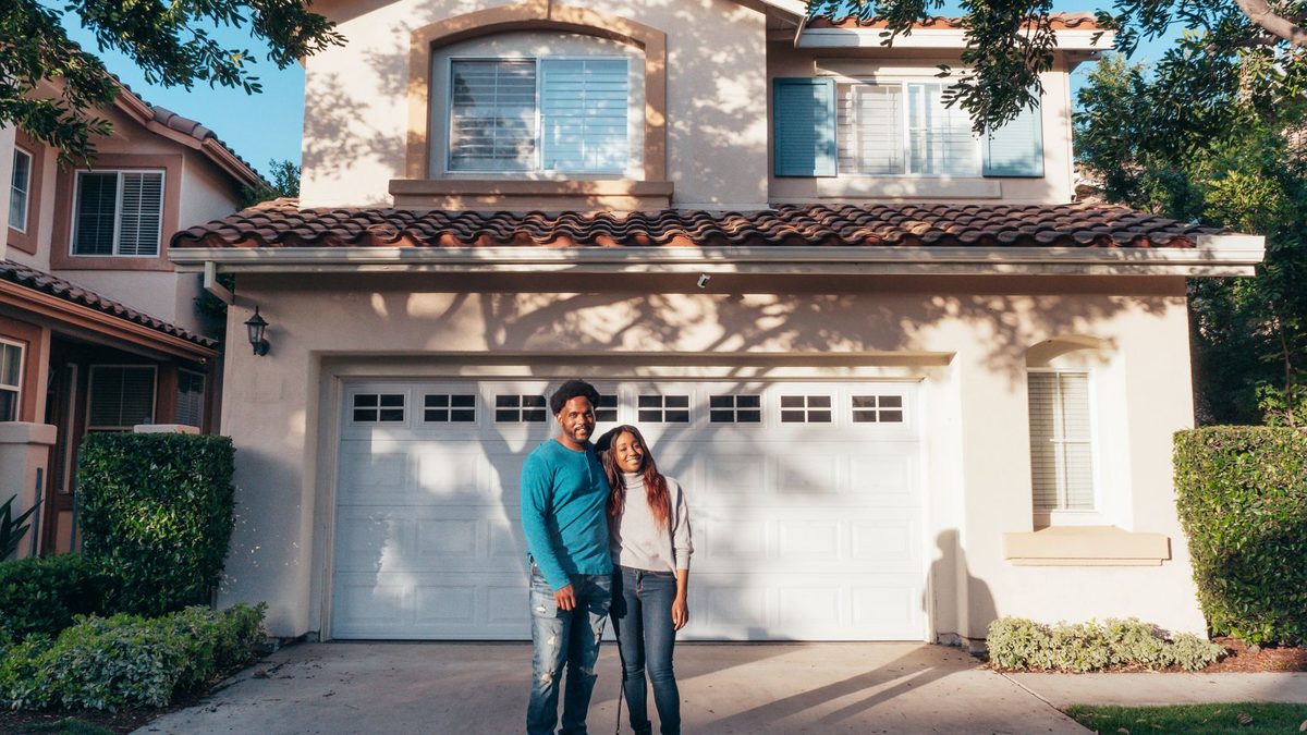 A joyous couple stands together in front of their newly purchased house, symbolizing new beginnings.