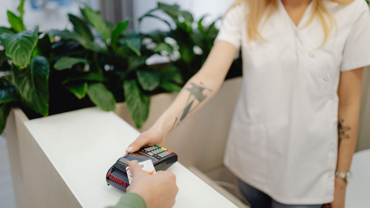 Tattooed staff member assists credit card payment in a clinic setting.