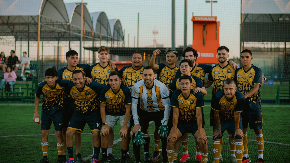 A soccer team poses together on a grassy field during daytime.