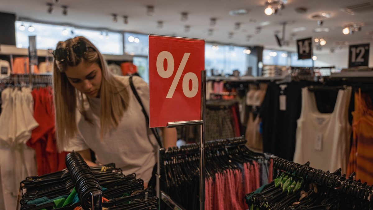 A young woman browses a clothing store during a sale, indicated by a red discount sign.