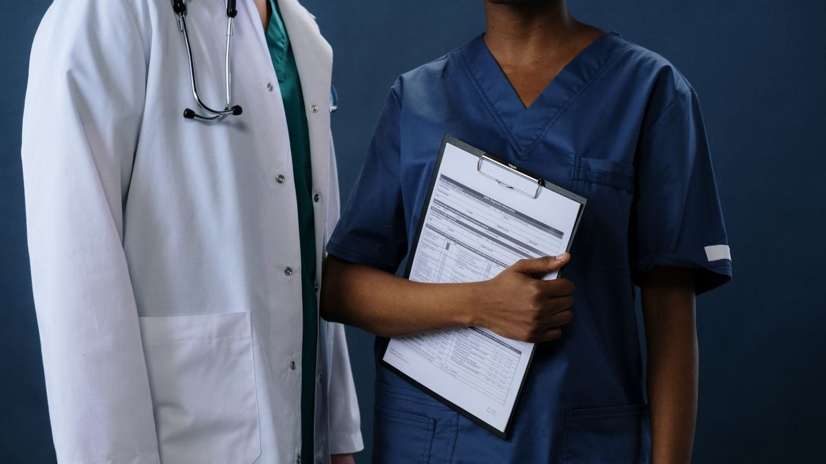 Two healthcare professionals in scrubs and lab coat with a clipboard, representing teamwork.
